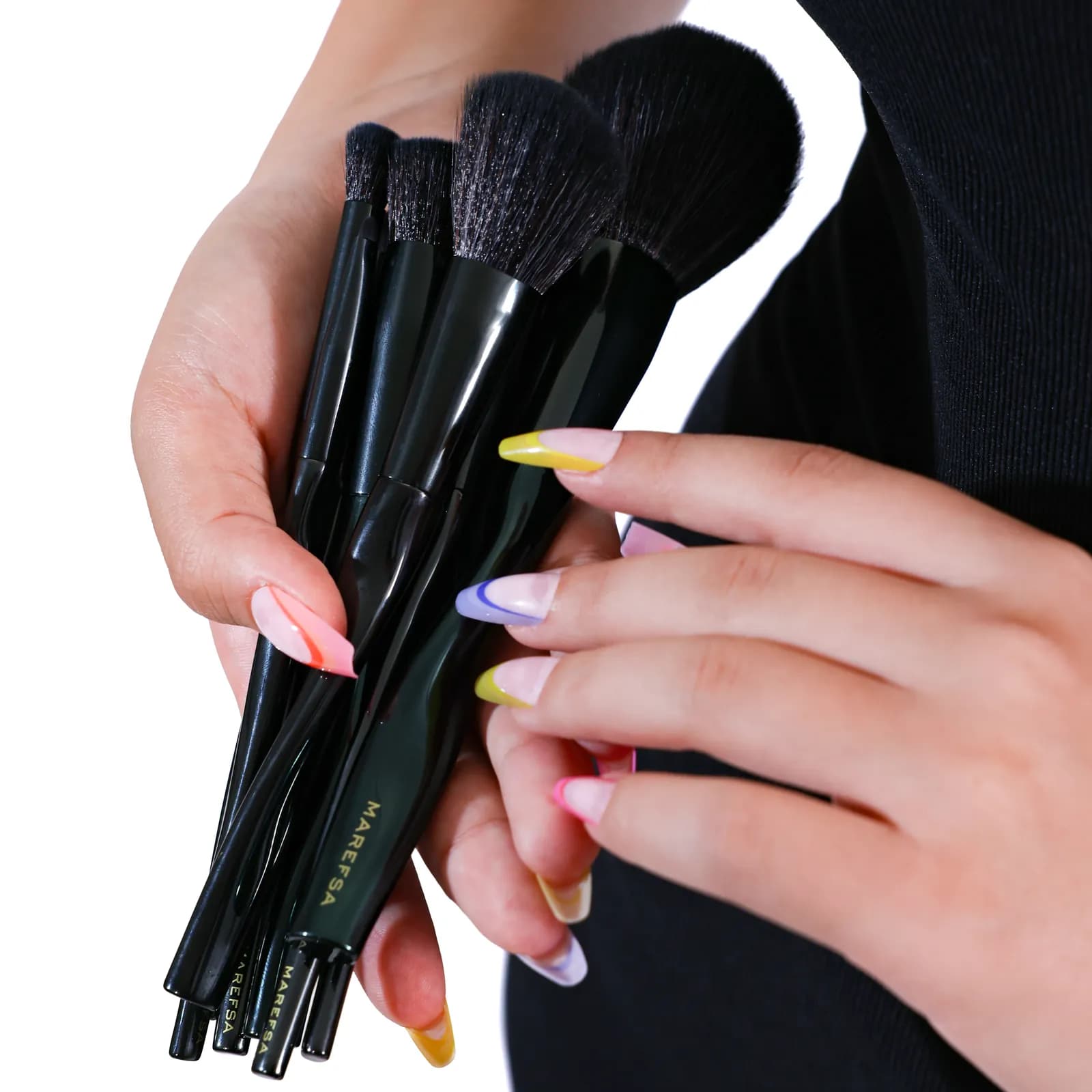 Hand holding the eight brushes of the Signature Brush Set against a black dress